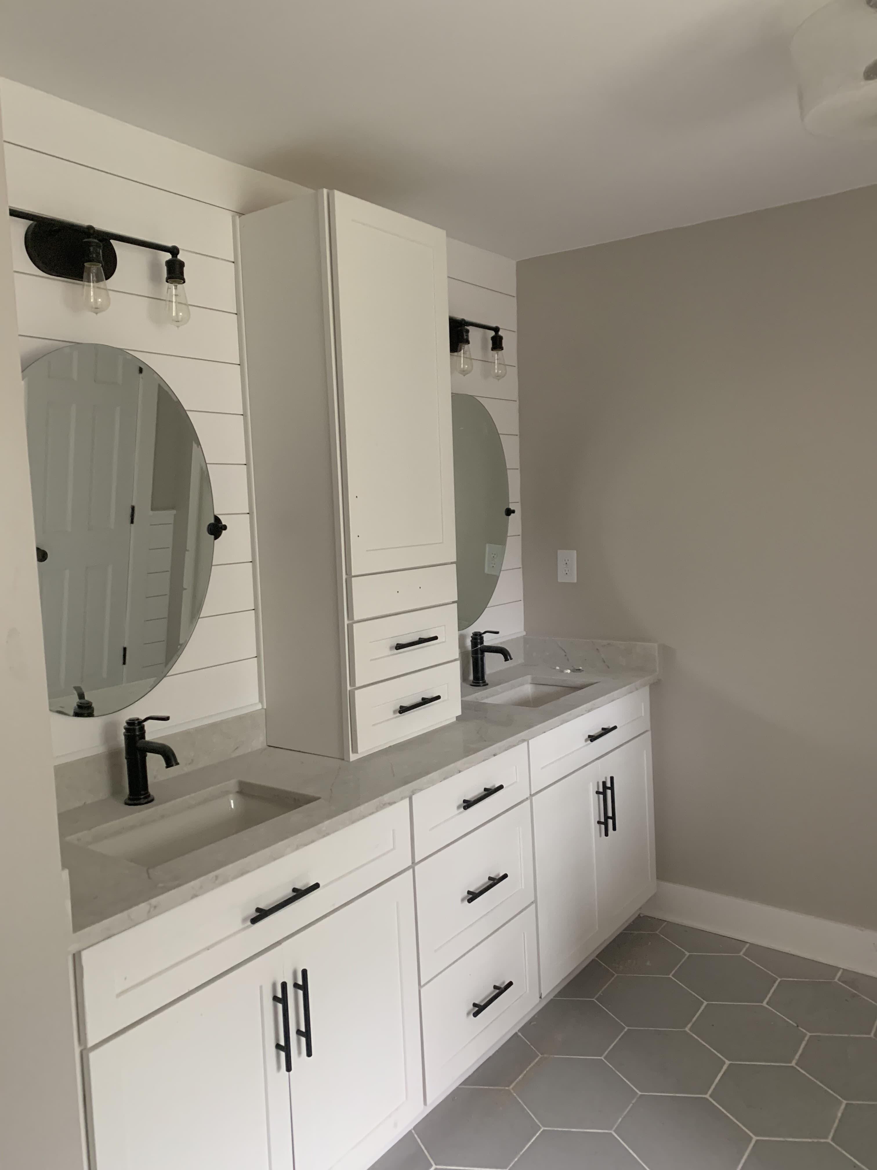 White double vanity with round mirrors, black fixtures, marble countertops, and hexagon floor tile
